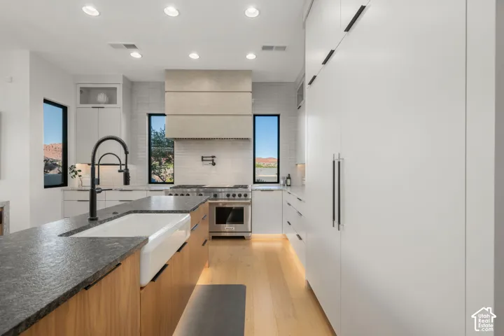 Kitchen featuring a large island with a farmhouse sink, stone countertops, and wood-finish cabinetry
