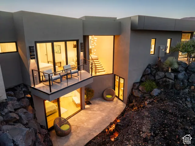 Multi-level modern exterior with a private balcony, ground-level patio, full-height windows, and integrated outdoor lighting