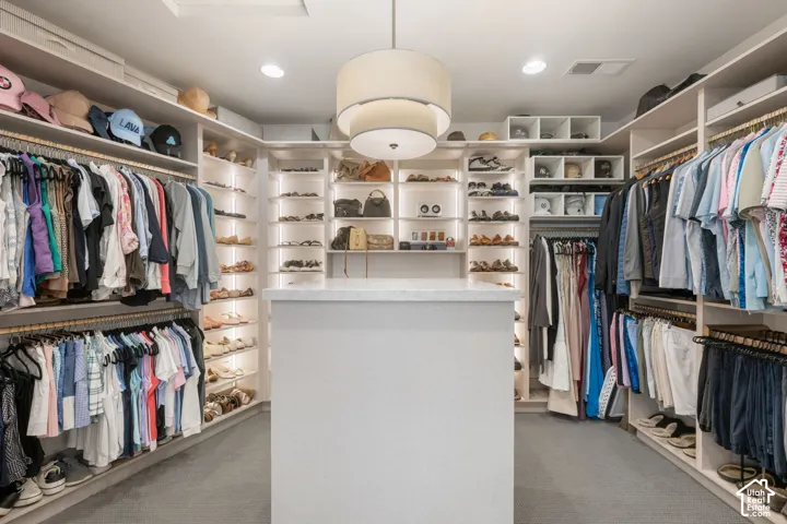 Custom closet system with extensive shelving, built-in storage, a central island with a solid surface countertop, and integrated lighting