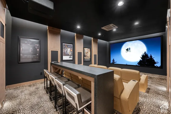 Dedicated media room featuring a large projection screen, recessed ceiling lighting, and a built-in bar with seating