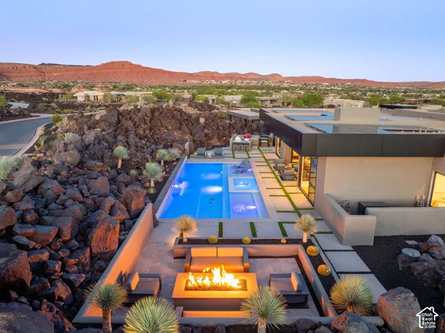 Outdoor patio featuring a rectangular pool and integrated spa, a fire pit, paver hardscaping, and desert landscaping