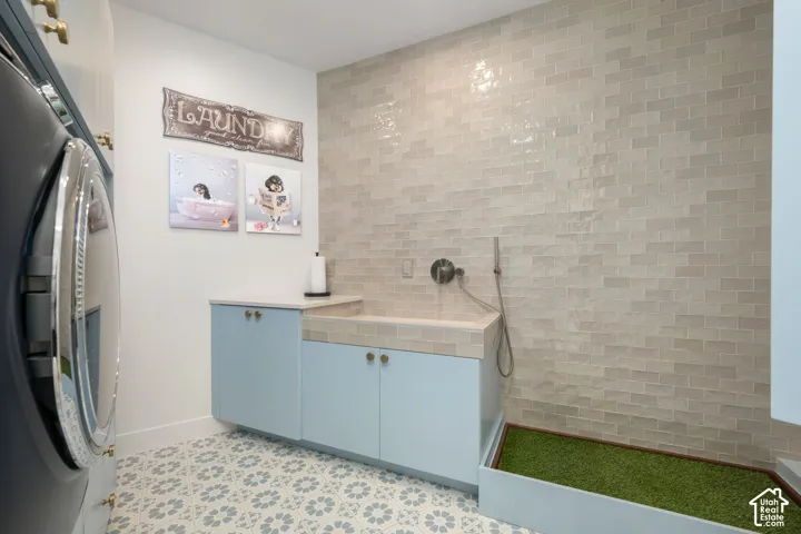 Laundry area featuring patterned floor tiles, light blue cabinetry, and a subway-tiled wall