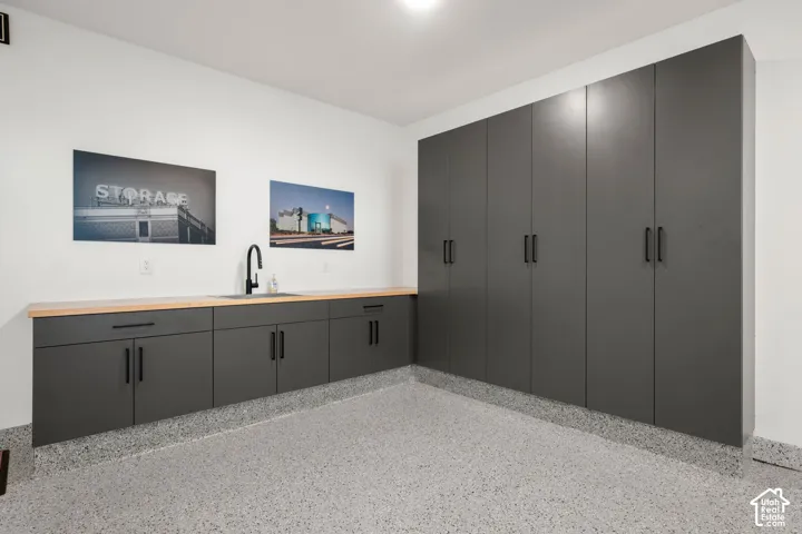 Extensive built-in cabinetry with matte black hardware, integrated sink with matte black faucet, wood-finish countertop, and durable speckled flooring