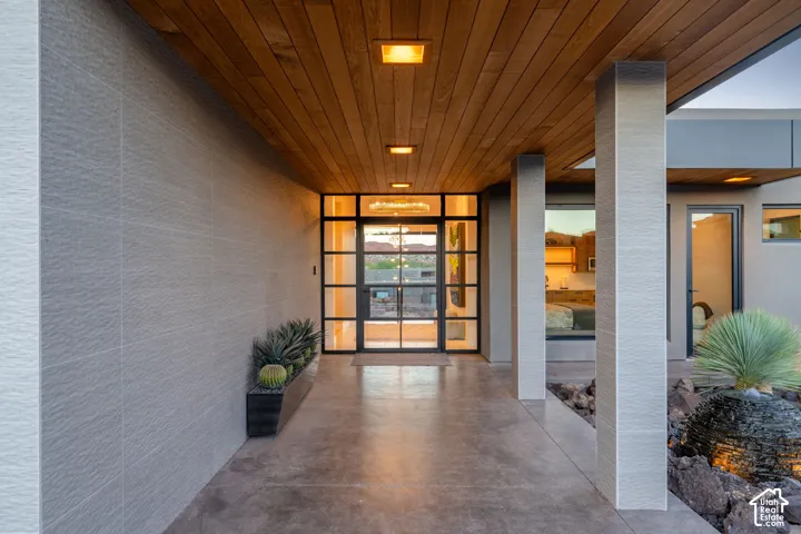 Wood-finish ceiling panels with recessed lighting, full-light entry door with grid detailing, textured wall panels, concrete flooring, and built-in landscape planter