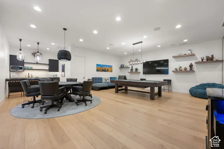 Spacious entertainment area featuring light wood-finish flooring, recessed lighting, a built-in wet bar with dark cabinetry, and floating wall shelves