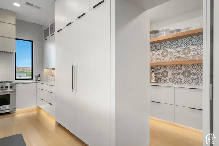Integrated panel-front refrigerator, stainless steel range, light wood-finish flooring, full-height white cabinetry, and patterned tile backsplash in the pantry