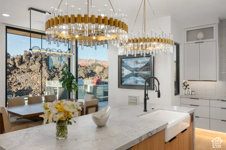 Modern kitchen island with a farmhouse sink, contemporary pendant lighting, light wood-finish cabinetry, and white tile backsplash