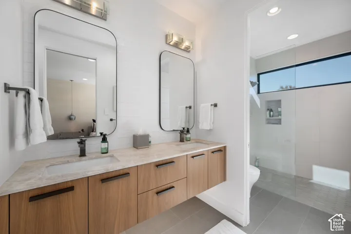 Floating wood-finish vanity with dual integrated sinks, stone countertop, black framed mirrors, and recessed overhead lighting