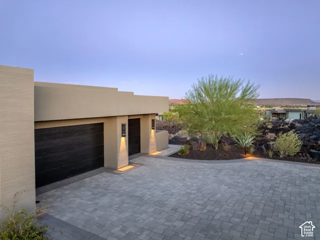 Paver driveway leading to dual dark wood-finish garage doors, accented by wall-mounted exterior lighting