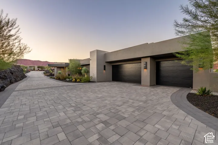 Stucco exterior with a paver driveway, two black garage doors, and landscape lighting