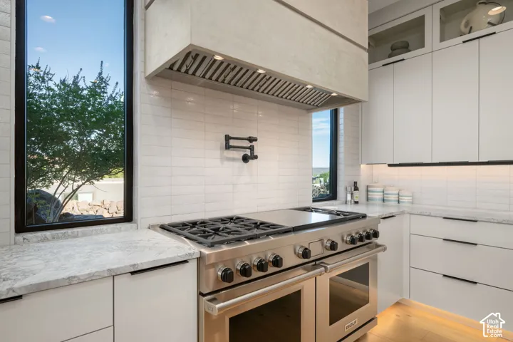 Stainless steel range with a built-in griddle, white cabinetry, integrated lighting, pot filler, and light-toned countertops