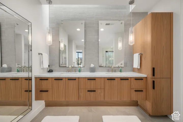 Dual sink vanity with wood-finish cabinetry, white countertop, and tile wall accents
