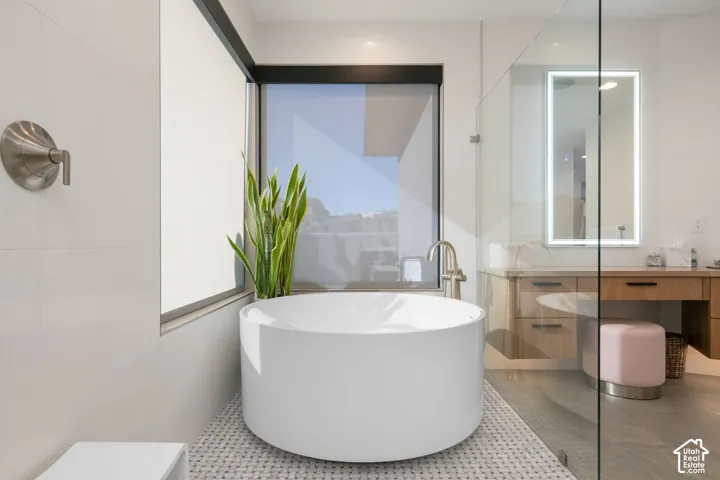 Freestanding soaking tub with floor-mounted brushed nickel faucet, large format tile walls, and a glass-enclosed shower with custom wood-finish vanity