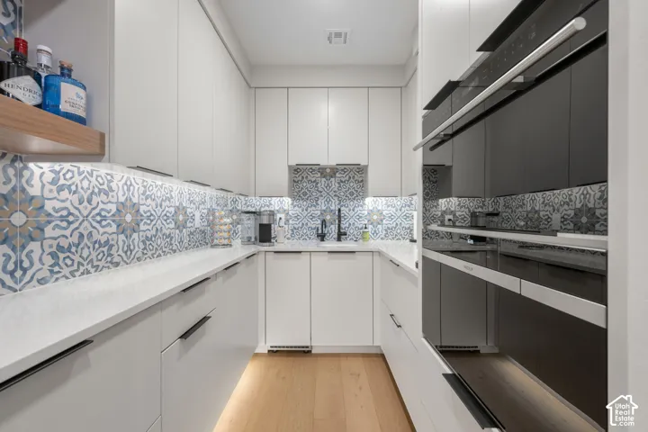 U-shaped kitchen featuring wood-finish flooring, white cabinetry with black pulls, tiled backsplash, white countertops, and integrated wall oven