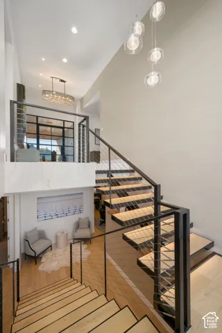 Open-tread staircase with metal and cable railing, wood-finish flooring, and a multi-tiered chandelier