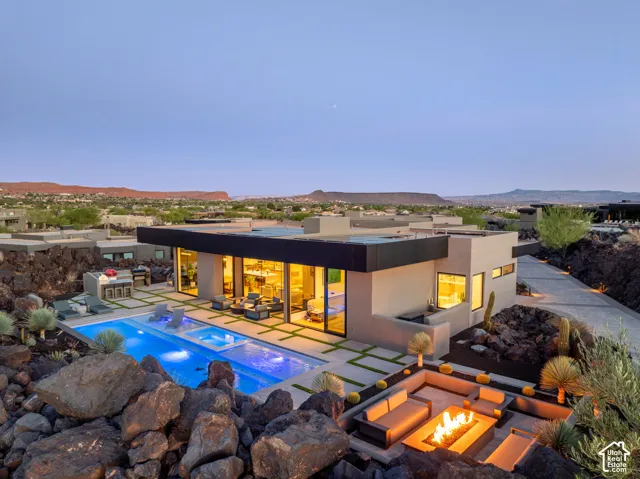 Modern exterior with expansive windows, an integrated swimming pool, a built-in outdoor kitchen, a sunken fire pit, and extensive hardscaping