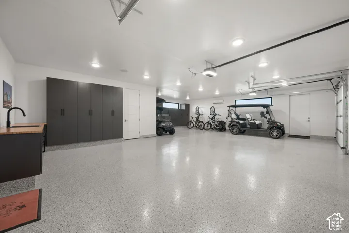 Epoxy flooring, extensive built-in cabinetry, wall-mounted air conditioning unit, ceiling-mounted lighting, and a utility sink with a black matte faucet