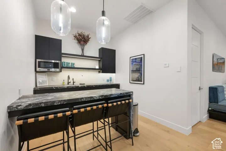 Integrated wet bar featuring dark cabinetry, stone countertops, and under-cabinet lighting