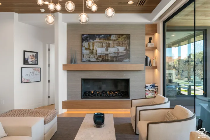 Wood-finish ceiling with integrated lighting, tiled fireplace surround, floating wood mantel, built-in fireplace, and sliding glass panel door