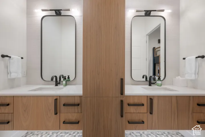 Dual vanity with wood-finish cabinetry and matte black hardware, integrated sinks, white countertops, and individual rectangular framed mirrors with task lighting
