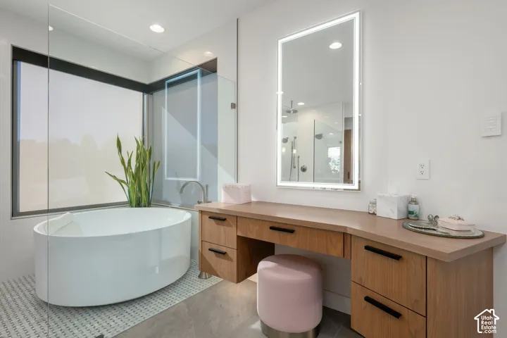 Freestanding oval bathtub, custom wood-finish vanity with integrated makeup area, illuminated vanity mirror, and large window with roller shade