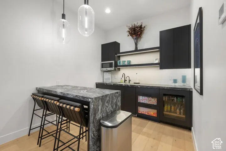 Wet bar featuring a waterfall counter, undermount sink, built-in beverage refrigerators, microwave, and open shelving with integrated lighting