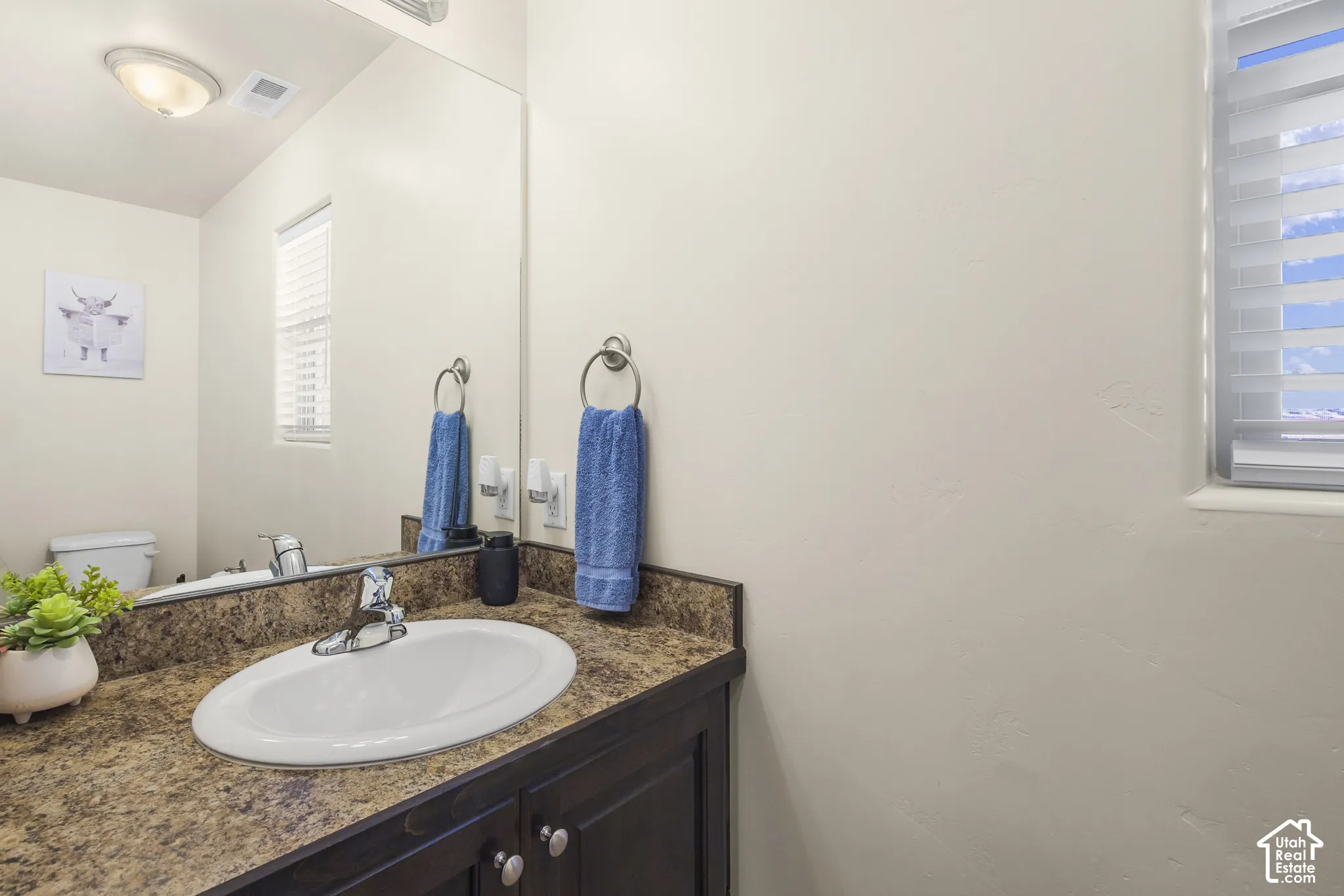 Vanity with an integrated sink, patterned countertop, dark wood-finish cabinetry, and a framed mirror