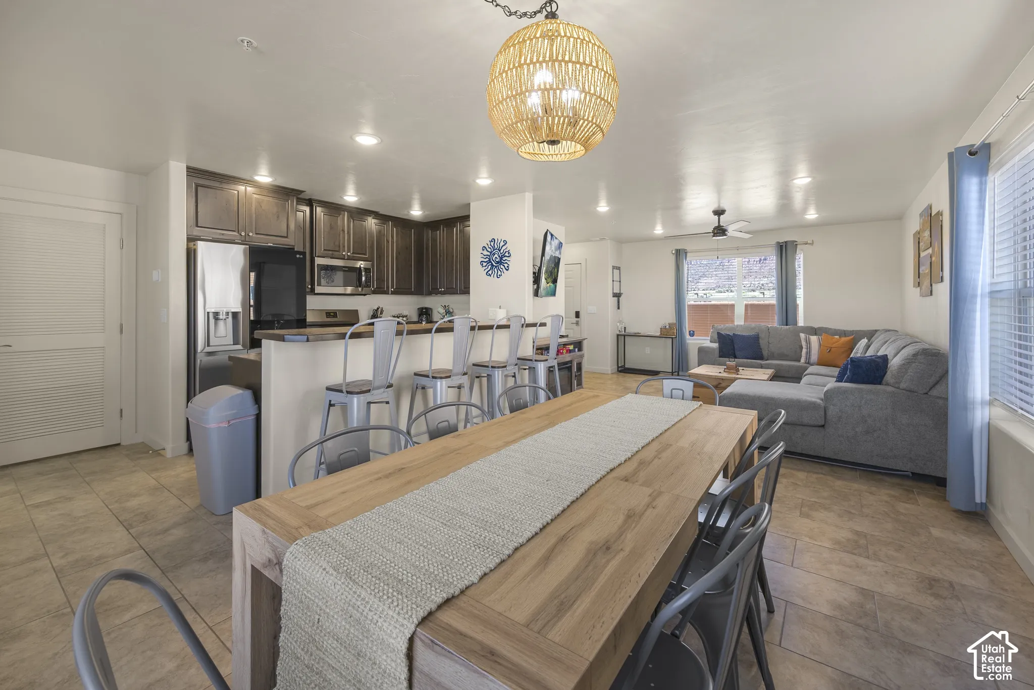 Open-concept living space with tile flooring, a kitchen featuring dark wood cabinetry and stainless steel appliances, and a breakfast bar with seating