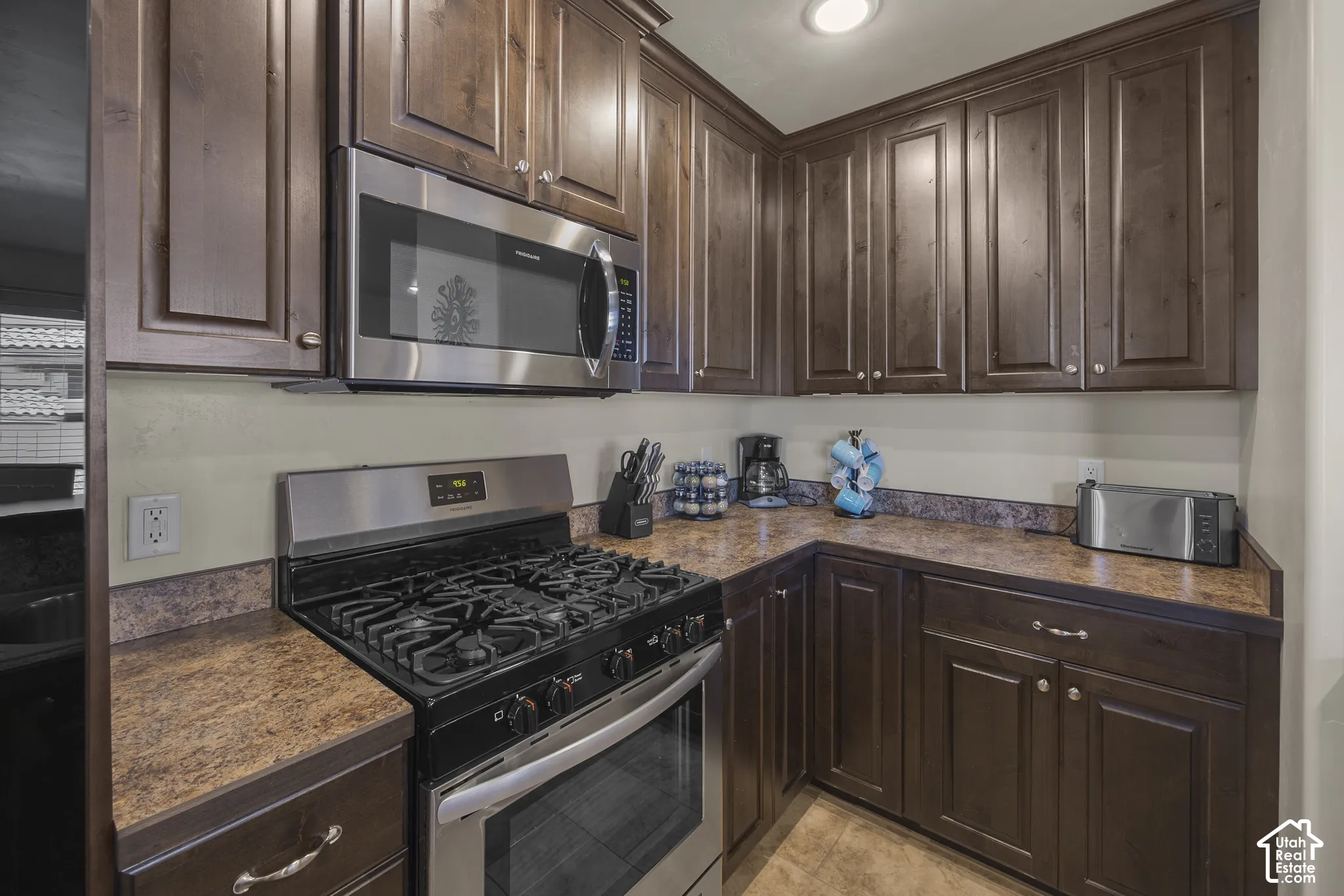 Built-in stainless steel microwave, dark wood-finish cabinetry, stainless steel range with gas burners, and patterned countertops