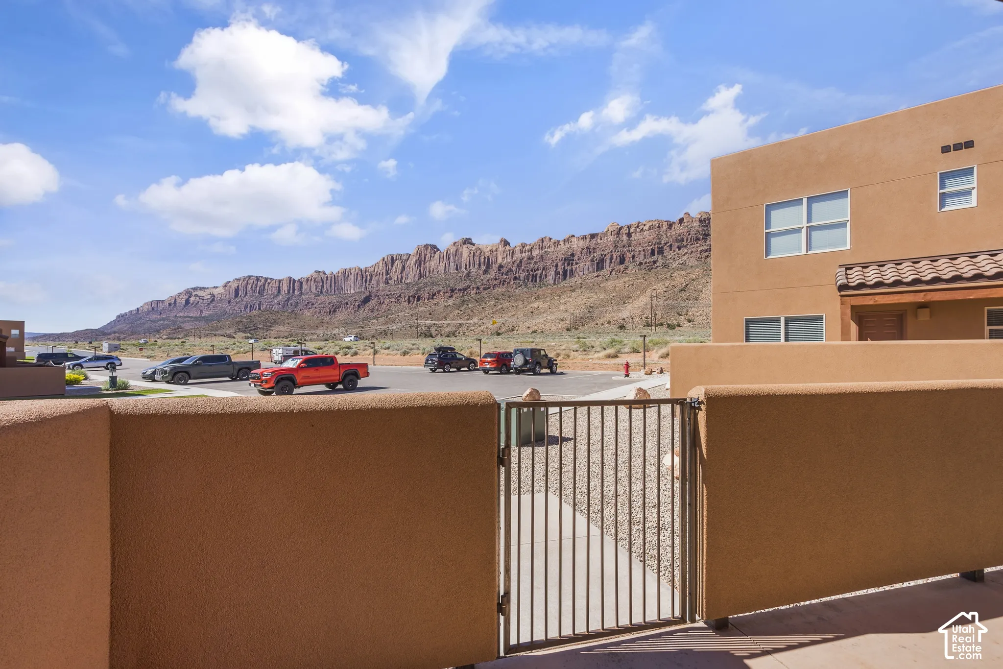 Exterior stucco finish, wrought iron gate, tiled roof accent, exposed wood beam detail, distant mountain scenery