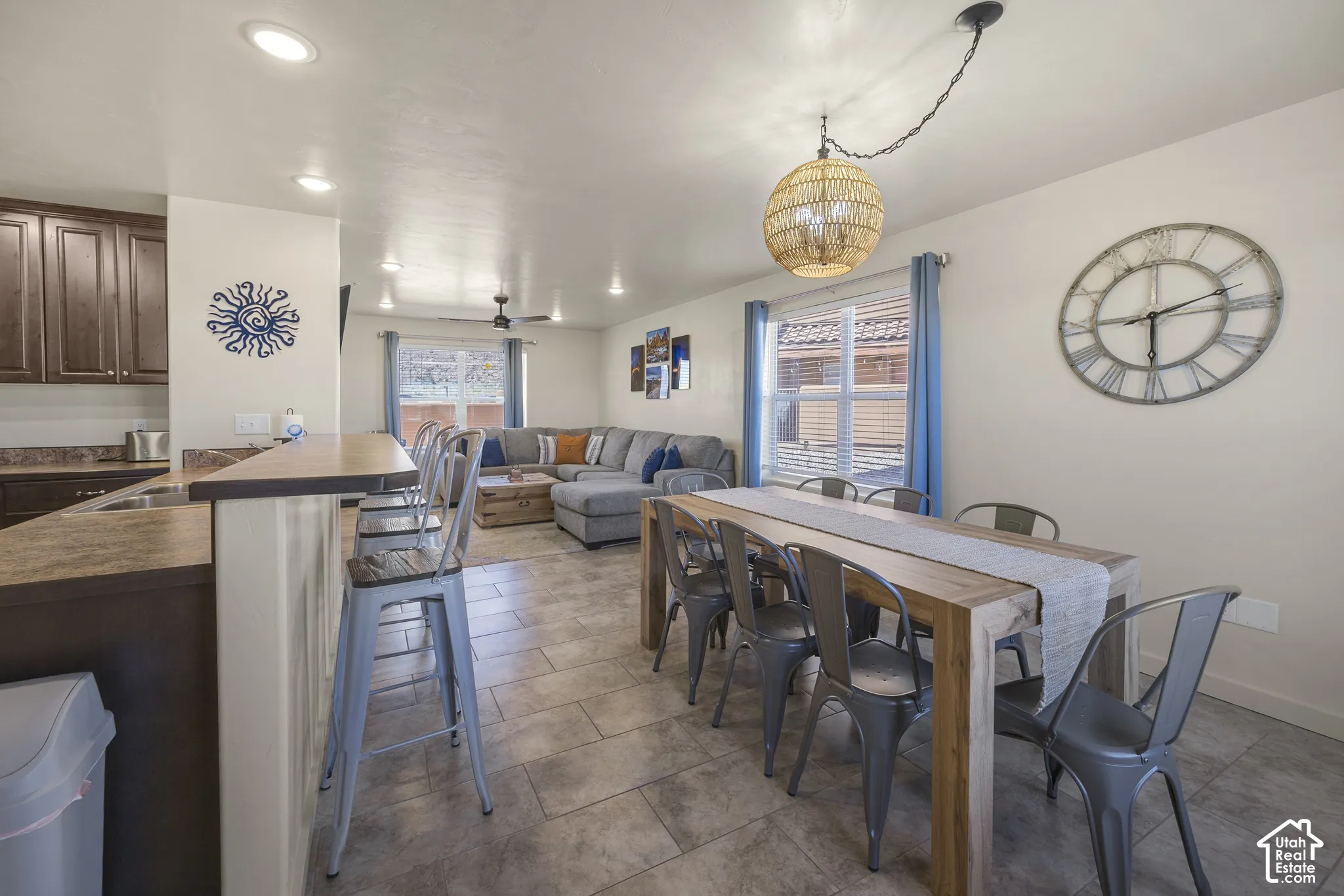 Open-concept living space with tile flooring, a kitchen featuring wood-finish cabinetry, and a dining area with a woven pendant light fixture