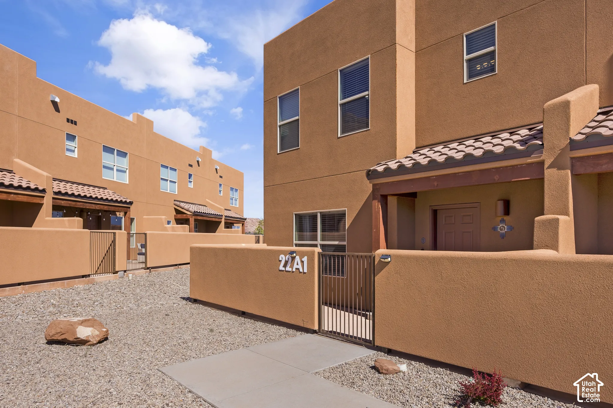 Stucco exterior with tile roof detailing, multiple windows, and a private gated courtyard entrance
