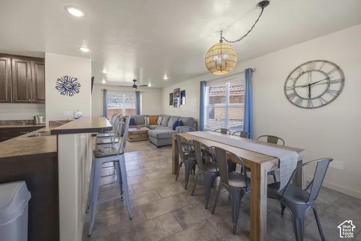 Open-concept living space with tile flooring, a kitchen featuring wood-finish cabinetry, and a dining area with a woven pendant light fixture
