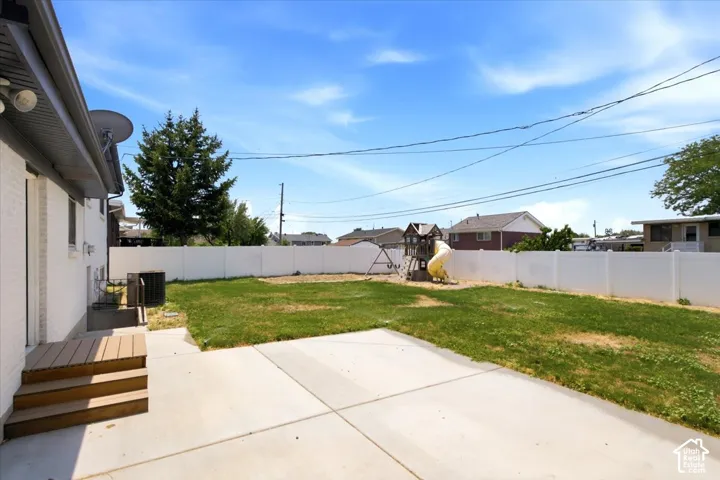 Expansive backyard featuring a concrete patio, wood-finish deck with steps, and a white privacy fence