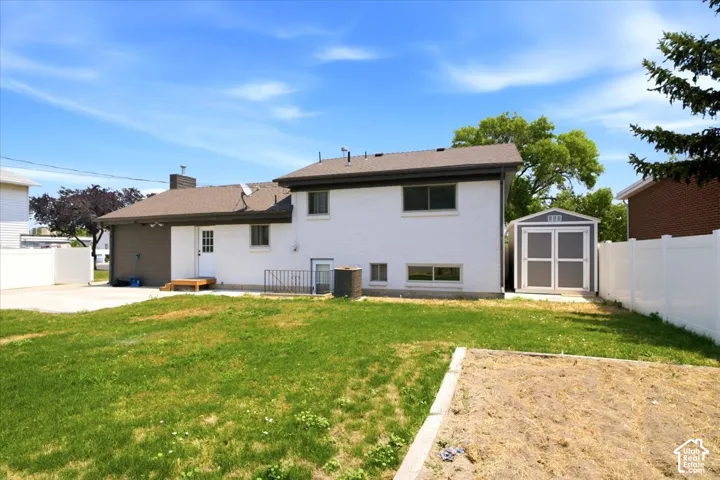 Expansive backyard with a manicured lawn, white vinyl fencing, a detached storage shed, and a concrete patio
