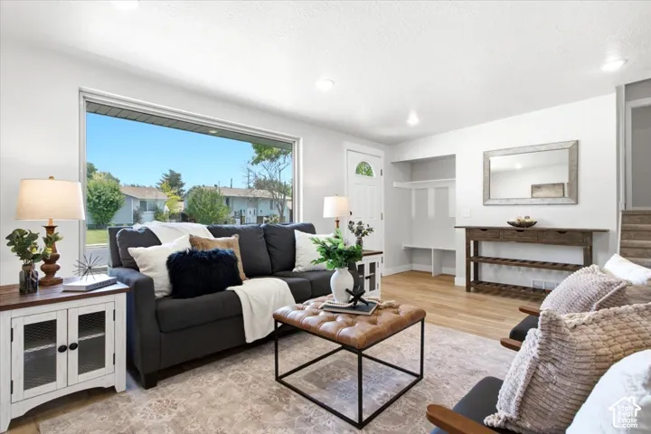 Spacious living area featuring a large picture window, light wood-finish flooring, recessed lighting, built-in coat rack, and a paneled entry door