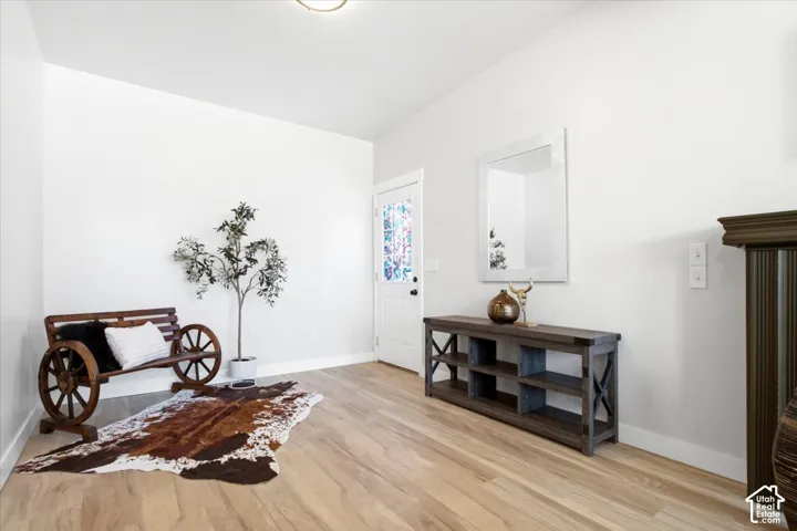 Vaulted ceiling, light wood-finish flooring, white walls, white trim, and a door with decorative glass