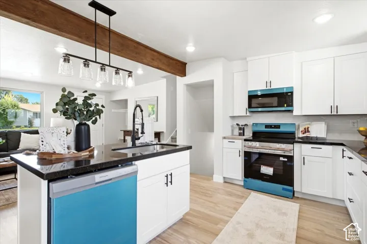 White cabinetry with matte black hardware, dark countertops, wood-finish flooring, and a decorative wood beam