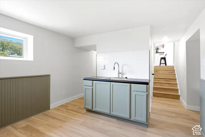 Light wood-finish flooring, white walls, and a built-in wet bar with a stainless steel sink and matte black countertop