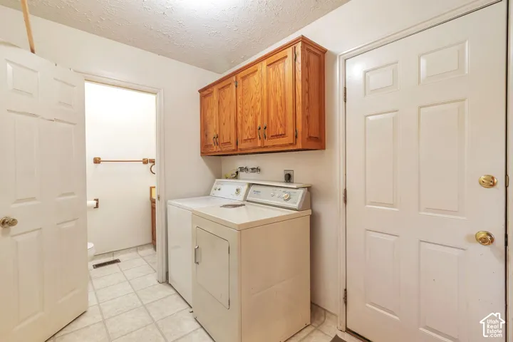 Functional laundry area featuring upper wood cabinetry and tile flooring