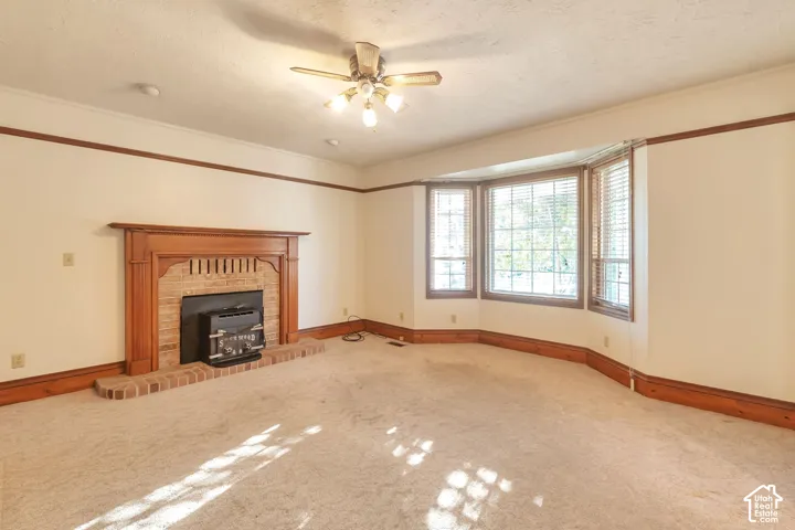 Fireplace featuring a brick surround and wood mantle, bay window, ceiling fan with light fixture, and wood trim detailing