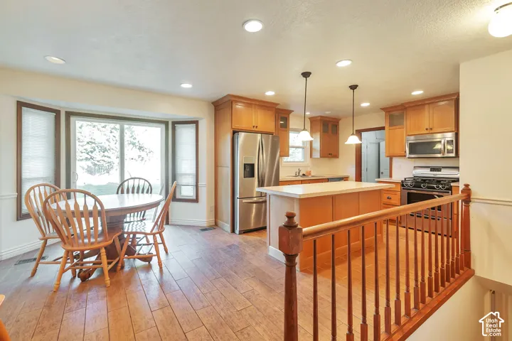 Kitchen with wood-finish flooring, light wood cabinetry, stainless steel appliances, and a central island with pendant lighting
