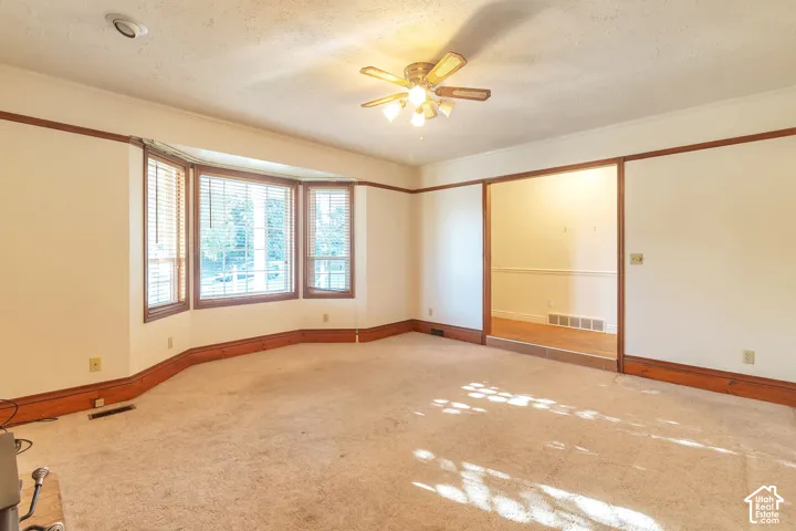 Expansive carpeted room featuring a bay window, wood trim, ceiling fan with light, and recessed lighting