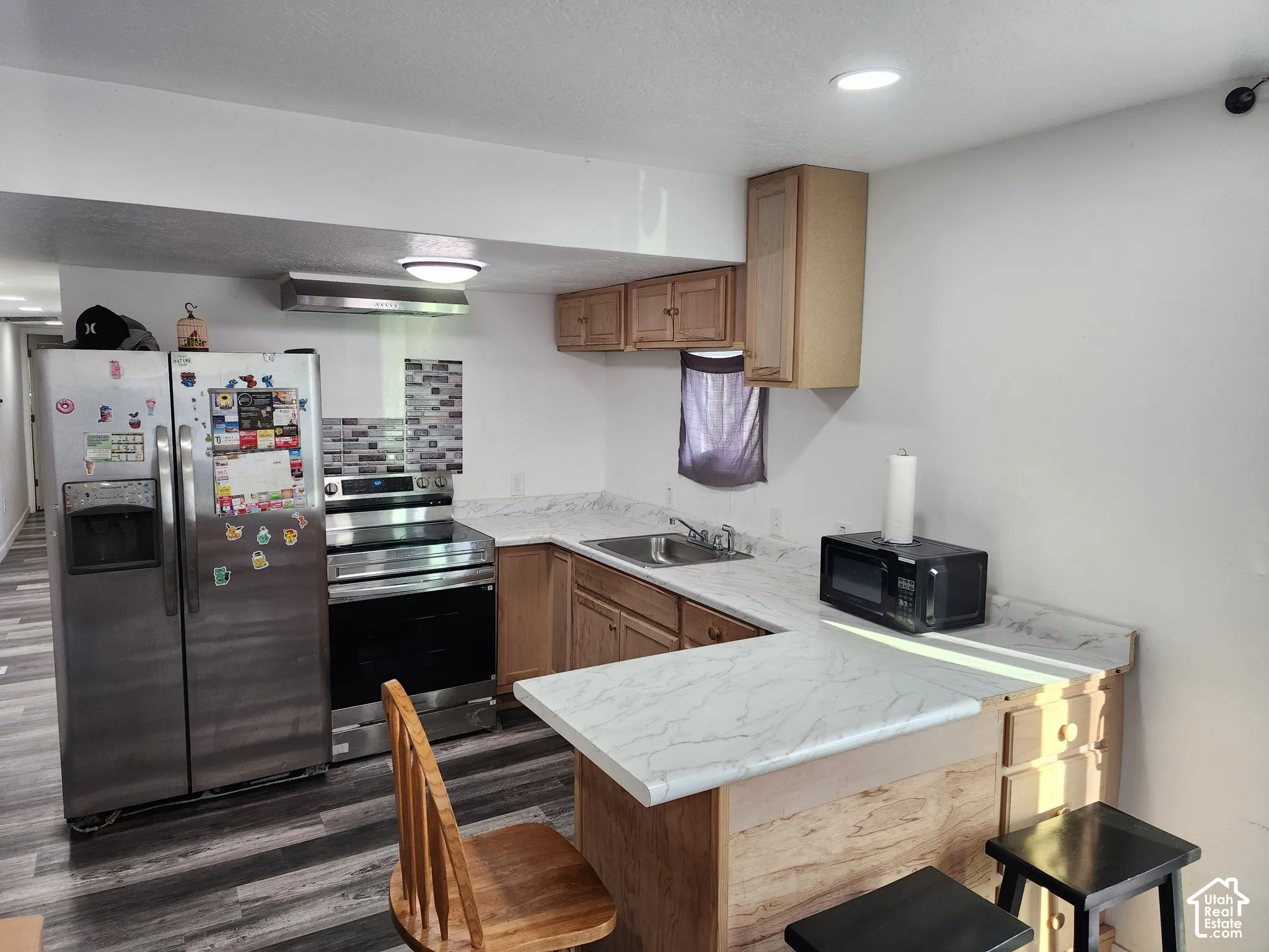 Kitchen featuring wood-finish flooring, stainless steel appliances, wood cabinetry, and a textured tile backsplash