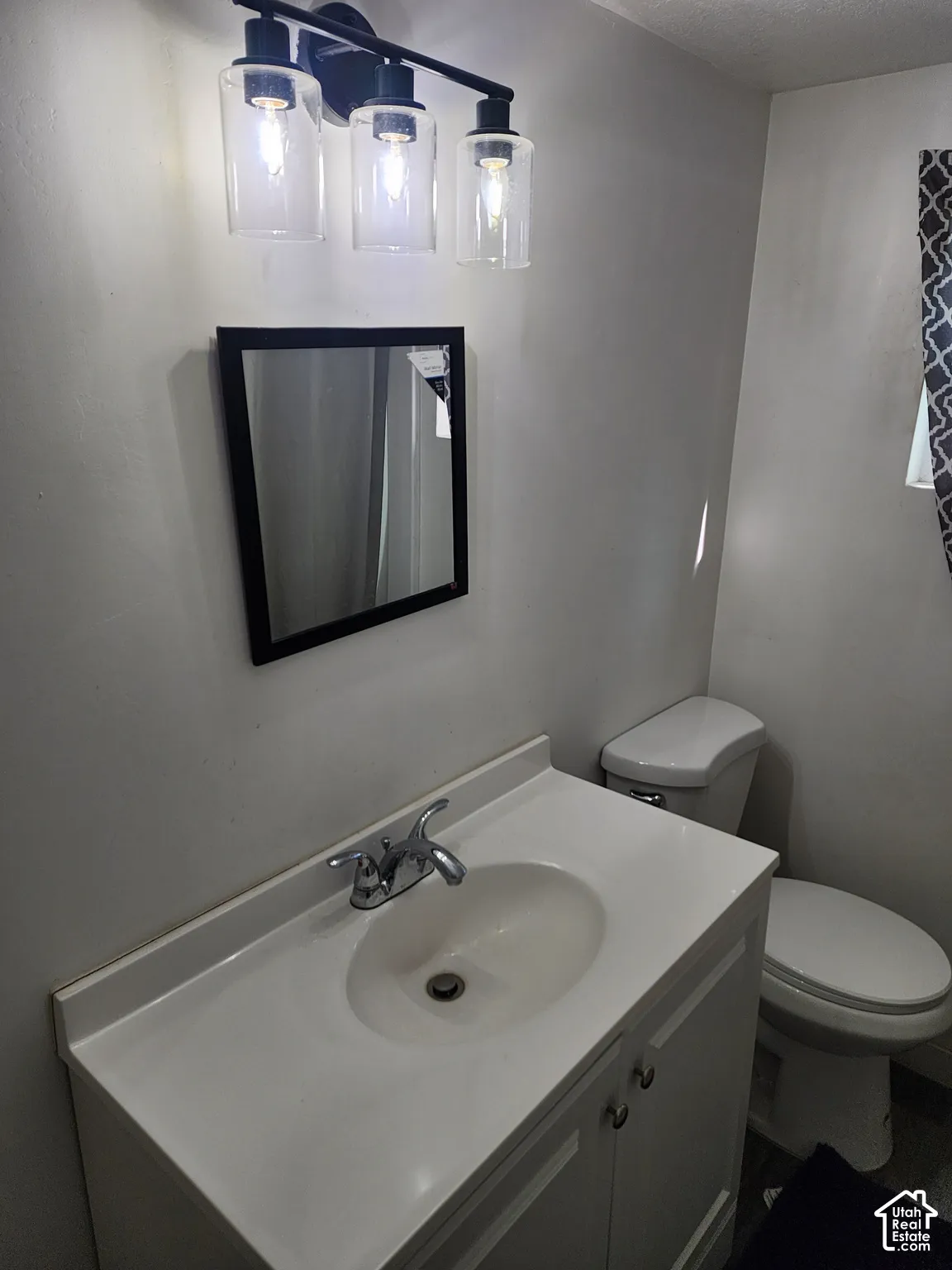 Vanity with integrated sink, chrome faucet, wall-mounted mirror, three-light vanity fixture with clear glass shades, and white toilet