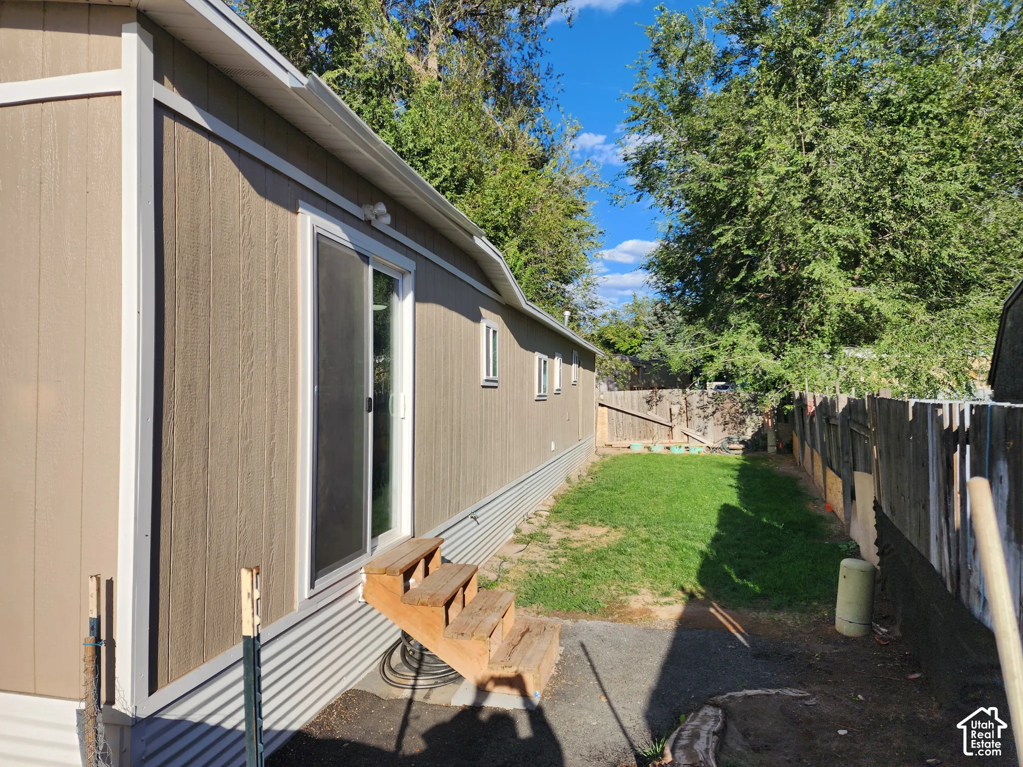 Sliding glass door access, wood steps, and a fenced backyard with a grass lawn