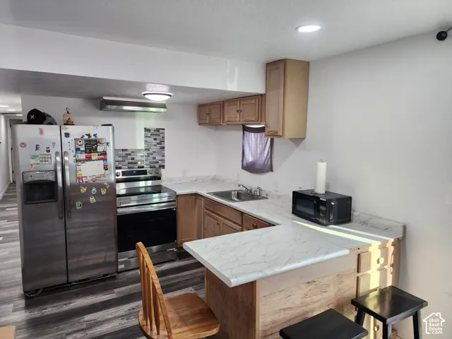 Kitchen featuring wood-finish flooring, stainless steel appliances, wood cabinetry, and a textured tile backsplash