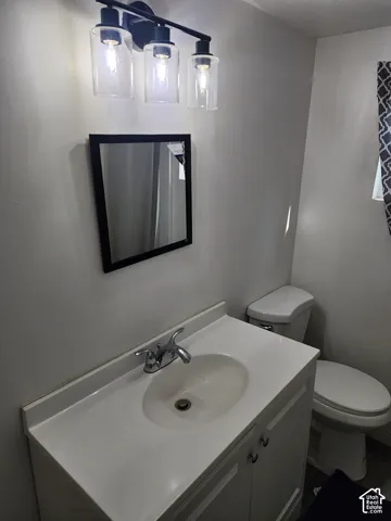 Vanity with integrated sink, chrome faucet, wall-mounted mirror, three-light vanity fixture with clear glass shades, and white toilet