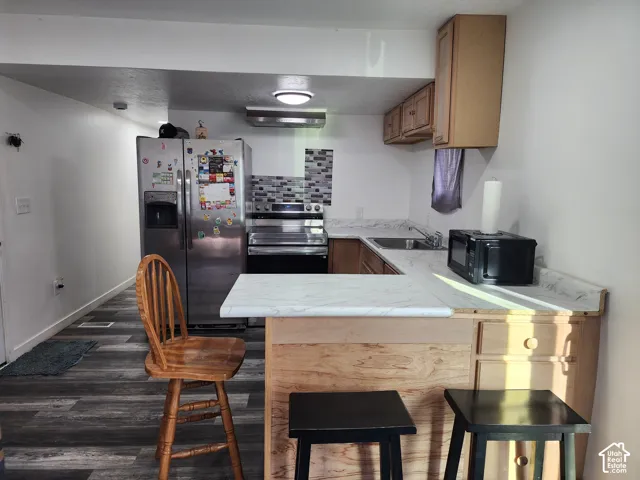 Kitchen featuring wood-finish flooring, stainless steel appliances, a mosaic tile backsplash, and light-toned cabinetry