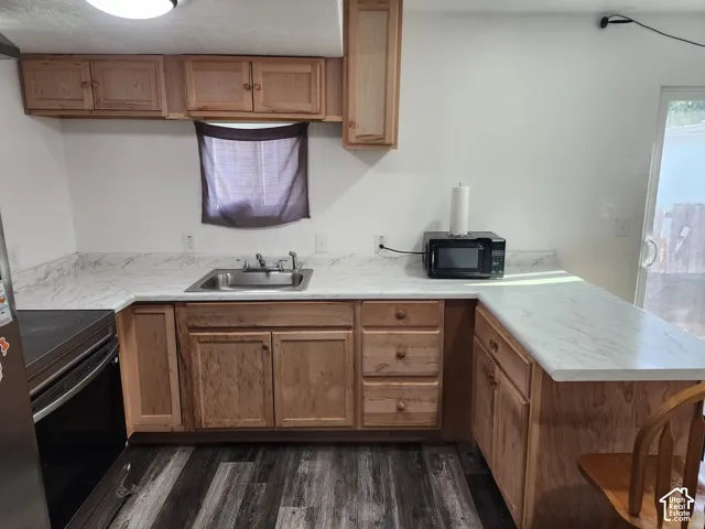 U-shaped kitchen layout with wood cabinetry, light-toned countertops, stainless steel sink, and wood-finish flooring